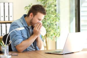 Man working in his home office while sneezing into a tissue from allergies